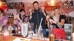 Teilnehmerinnen eines Junggesellinnenabschieds stehen mit Markus hinter der Bar und schütteln Cocktails